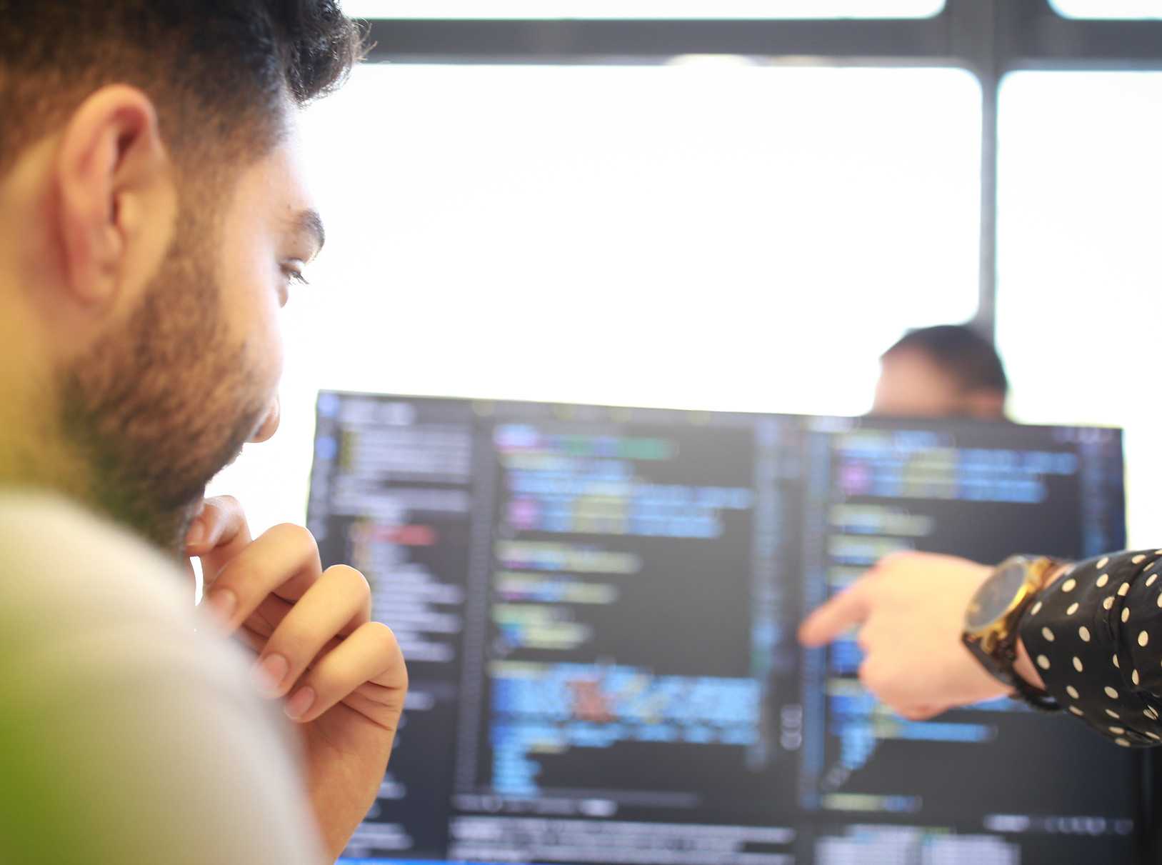Programmierer schaut auf Monitor mit Quellcode. Eine Kollege zeigt auf den Monitor.